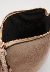 Pochette in pelle beige con texture, chiusa da una zip dorata, aperta per rivelare un interno in tessuto nero con una tasca zip interna più piccola.
