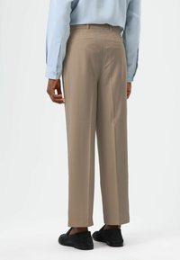 Beige trousers made from smooth material, featuring a straight leg design, rear pockets, and a clean finish. Paired with black shoes.