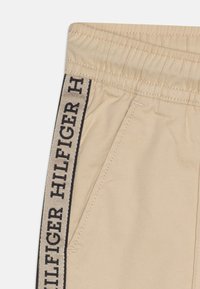 Beige joggingbroek met een elastische tailleband, zijzakken, en een zwarte logotape langs de zijkant met contrasterende stikseldetails.