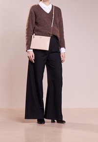 Beige leather crossbody bag with a gold chain strap, paired with a brown wool sweater and black wide-leg trousers. White collared shirt underneath.