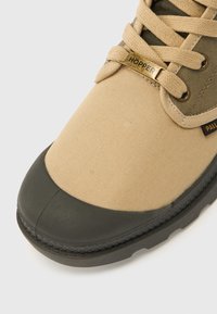 Μπεζ και ελιάς πράσινο μποτάκι με κορδόνια, μαύρο λαστιχένιο κάλυμμα μύτης, μεταλλική ταμπέλα κορδονιών με το λογότυπο "HOPPER" και υφασμάτινη ετικέτα "PALL" κοντά στα κορδόνια.