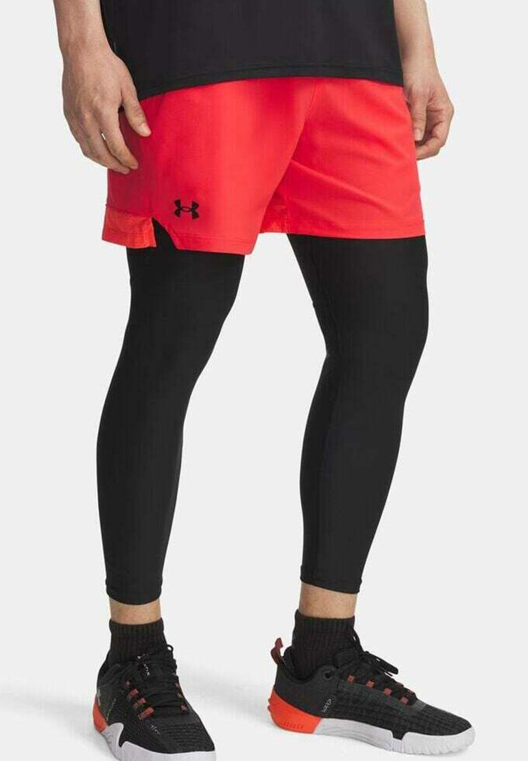 Zwarte compressie leggings gecombineerd met felrode sportshorts. Kenmerken omvatten een logo op de shorts en zwarte sportschoenen met rode accenten.