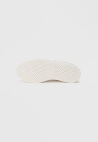 Semelle de sneaker blanche avec un grip texturé et à motifs. Le design présente une forme arrondie et est principalement lisse avec des détails de marque subtils.