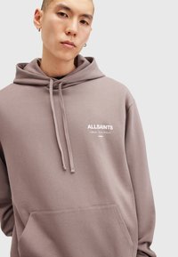 Grå hætte Sweatshirt med snøre, stor frontlomme og hvid logo tekst på brystet. Fremstillet af blødt, tekstureret stof.