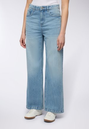 Jeans azzurri chiari a gamba larga con un lavaggio sbiadito, caratterizzati da un design a cinque tasche e chiusura con bottone, abbinati a sneakers bianche.