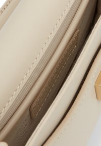 Vnitřek béžové kožené kabelky se zipovou kapsou a jemným švem. Hladký povrch s viditelnou malou akcentovou etiketou.