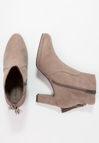 Taupe Wildleder-Stiefeletten mit Blockabsatz, seitlichem Reißverschluss und Quasten-Detail. Glatte Textur mit einem runden Zehendesign.