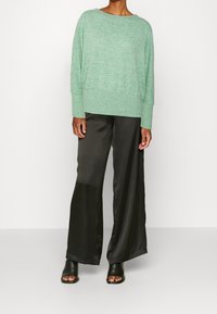 Mintgrön stickad tröja med vid halsringning och lös passform, kombinerad med högmidjade svarta satinbyxor med vida ben och svarta slidesandaler.