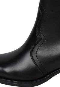 Bottine en cuir noir avec une texture lisse, des détails de couture courbés et un bout arrondi ; elle présente une semelle noire basse et solide.