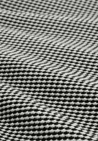 Schwarzes und weißes Hahnentrittmuster-Gewebe mit strukturierter Webart, das einen subtilen Glanz und eine sanfte, taktile Oberfläche aufweist.