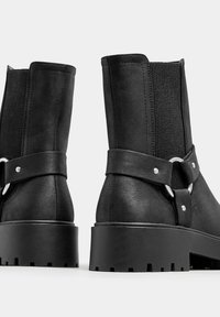 Black ankle boots with elastic side panels, smooth upper material, sturdy block heel, and metal accents on a strap.