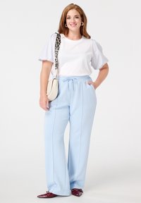Pantalon large bleu clair avec taille à cordon, associé à un haut blanc avec des manches bouffantes rayées et des chaussures bourgogne. Sac bandoulière beige.