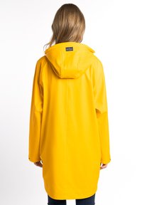 Sárga vízálló esőkabát kapucnival, laza fit-tel és hosszú ujjakra tervezve. A hátsó nézet sima textúrát és minimális hardvert mutat.
