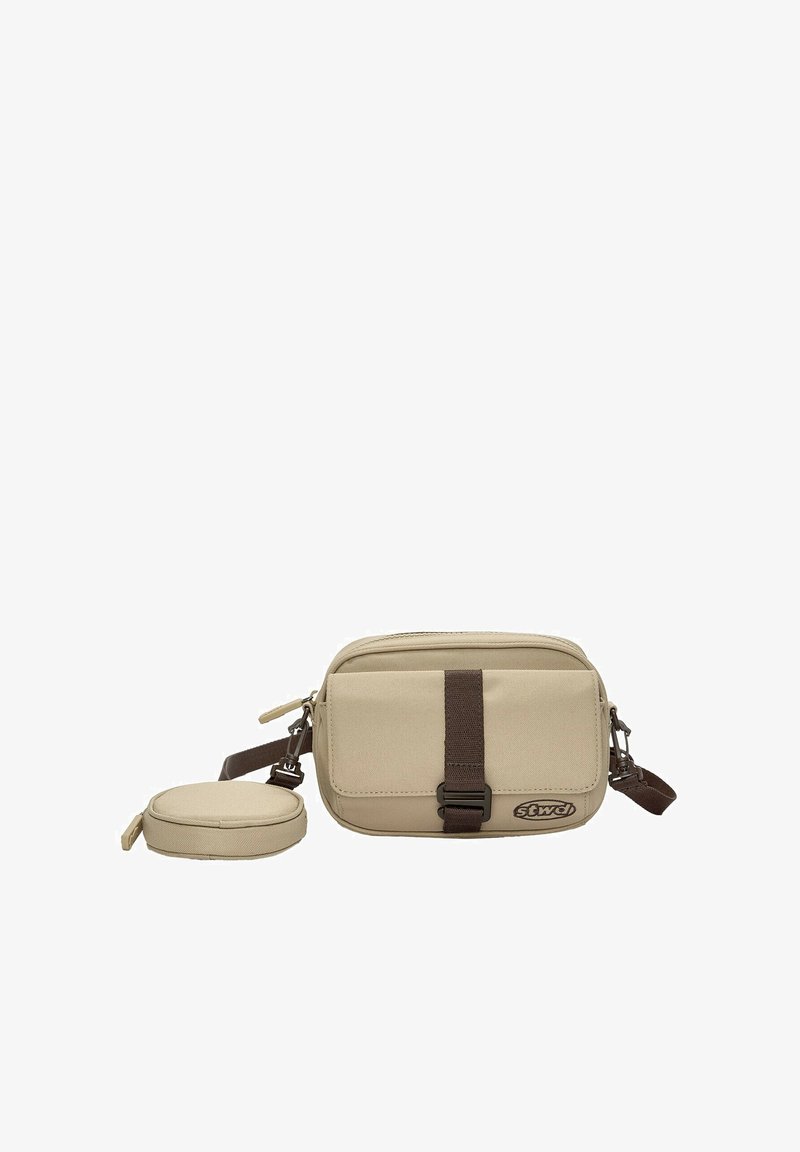 Beige kangaskassi, jossa on ruskea olkahihna, edessä vetoketjusäilytys ja pyöreä pussi. Yksinkertainen suorakaiteen muotoinen, kevyt muotoilu.