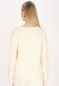 Maglione sovradimensionato di colore crema, con una texture morbida, scollatura a costine e spalle cadenti. La vista posteriore mostra dettagli minimi e una vestibilità rilassata.