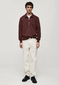 Burgundská mikina na zip s žebrovanými manžetami, kombinovaná s bílými chino kalhotami a černými šněrovacími botami. Minimalistický design, hladké textury.