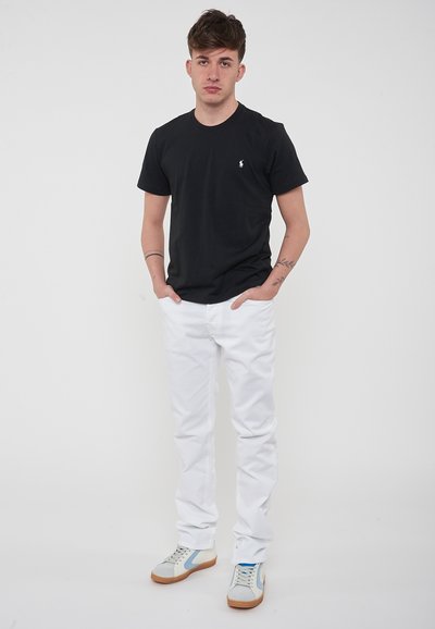 T-shirt in cotone nero con un piccolo logo bianco, abbinata a pantaloni in denim bianchi e sneakers multicolori. Design pulito, vestibilità casual.