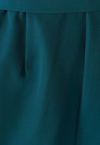 Sini-vihreä kangas on sileä ja hieman kiiltävä, jossa on hienovarainen laskeutuvuus, pehmeät laskokset ja poimut tuovat siihen elegantin ilmeen.