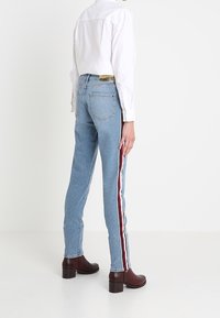 Jeansy z wysokim stanem w kolorze niebieskim, wykonane z dżinsu, z czerwonymi i białymi paskami po bokach, prostą nogawką, pięcioma kieszeniami oraz markową skórzaną metką na tylnym pasku.