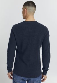 Pull en maille côtelée bleu marine à manches longues, col rond et poignets ajustés, porté avec un jean en denim.