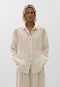 Cremefarbiges gestreiftes Shirt aus leichtem Stoff mit lässiger Passform, das eine Knopfleiste und eine einzelne Brusttasche aufweist.