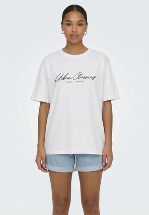 Kvinde iført en hvid oversize T-shirt med teksten "Urban Classics EST. 2005" og lyseblå optrukne denimshorts, vendt fremad.