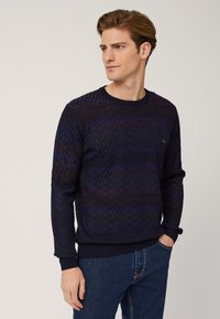 Maglione blu navy con motivo a zigzag, texture a maglia e scollatura a girocollo. Presenta maniche lunghe e polsi e orlo a costine.