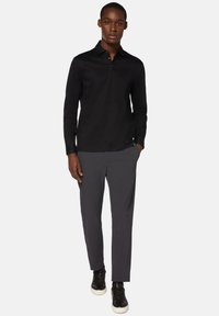 Czarna koszulka polo z długim rękawem i kołnierzykiem, z zapięciem na guziki, w połączeniu z szarymi spodniami i czarnymi trampkami z białymi podeszwami.