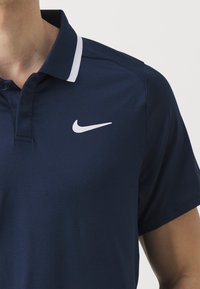 Dunkelblauses Poloshirt aus glattem Stoff mit einem weißen Nike-Logo auf der linken Brust und einem kontrastierenden weißen Streifen am Kragen.