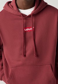 Bordeauxroter Hoodie aus Baumwollmix, mit einer Fronttasche, Kordelzügen und einem roten gestickten Levi's Logo auf der Brust.