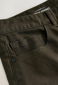 Olive roheline denim kangas lähivõte, millel on väike tagatasku musta nupuga ja kontrastsete õmblusdetailidega.