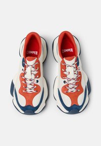 Scarpe da ginnastica rosse, bianche e blu con una tomaia texturizzata, dettagli in suede e un colletto imbottito; lacci decorati e una suola spessa.