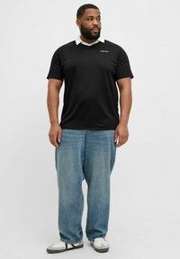 Svart kortärmad polo t-shirt med vit krage och vertikalt randigt mönster, kombinerat med ljusblå baggy jeans och vita sneakers.