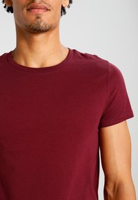 Camiseta de cuello redondo burdeos hecha de un suave tejido de algodón. Manga corta, diseño ajustado y costuras mínimas para un aspecto limpio.