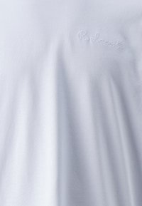 Camiseta blanca de algodón con un sutil logo bordado en hilo claro, textura suave y un ajuste relajado.