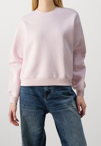 Rosa sweatshirt i mjukt tyg, med rund hals, långa ärmar och ribbad nederkant. Buren med mörkblå denimjeans.