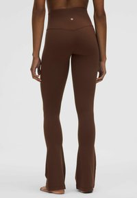 Brązowe legginsy o wysokim stanie w stylu dzwonów, wykonane z elastycznej tkaniny o gładkiej fakturze, z detalem logo blisko pasa, zaprojektowane z myślą o komforcie.