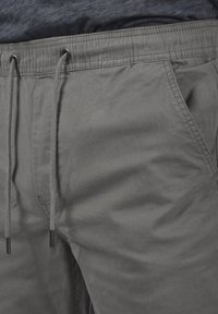 Pantalones grises de tejido suave, con cinturilla elástica y cordones, bolsillos laterales y un corte relajado.