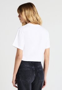 Maglietta bianca in cotone con maniche corte e scollatura rotonda, abbinata a jeans grigi scuri a vita alta con tasche posteriori.