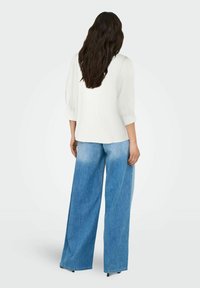 Hvid bluse med pufferærmer parret med højtaljede, brede blå denimjeans med en lys-til-mørk ombre-effekt ved kanten.