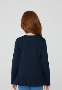 Granatowa bluzka z długim rękawem i okrągłym dekoltem, z falbaniastym dołem. Wykonana z miękkiego bawełnianego materiału o gładkiej fakturze, z dopasowanym krojem.