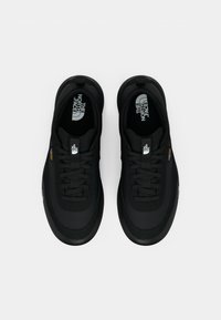 Black athletic shoes with a smooth fabric upper, round toe, thick rubber sole, and prominent logo branding on the insole and side.