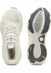 Zapatillas de correr blancas con una parte superior de malla texturizada, suela acolchada y una suela de goma flexible que presenta un patrón en zigzag y acentos.