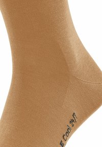 Chaussette beige avec une texture lisse et des côtes fines. Comprend le logo et les informations sur le produit près de la cheville. Conçu pour le confort et la respirabilité.