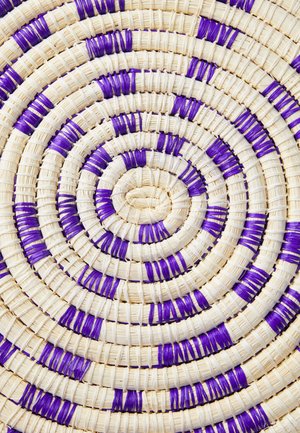 Kerek, krém színű szőnyeg lila díszítésekkel, koncentrikus körmintákkal és strukturált felszínnel.