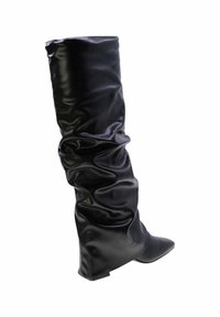 Stivale in pelle nera alto e sformato, con punta affilata e tacco basso, in posizione verticale su sfondo bianco.