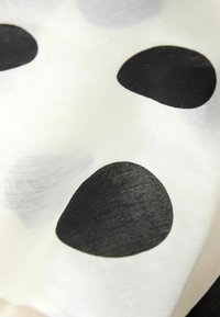 Tissu blanc avec de grands pois noirs irréguliers, montrant la texture et de légers plis dans le matériau.