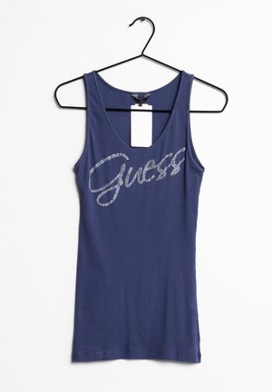 Top sin mangas de canalé en azul marino con un escote en V profundo y el logo de "Guess" en purpurina plateada en el pecho. Cuélga de una percha de alambre negra.