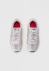 Nike tenisice za trčanje u sivoj mrežastoj tkanini s crvenim akcentima. Imaju bijele vezice, srebrne pruge i podstavljeni ovratnik. Istaknuti logo na jeziku.