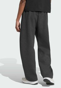 Sivé tepláky vyrobené z mäkkého materiálu, s voľným strihom a elastickým pásom. Osoba ich nosí s svetlými teniskami.